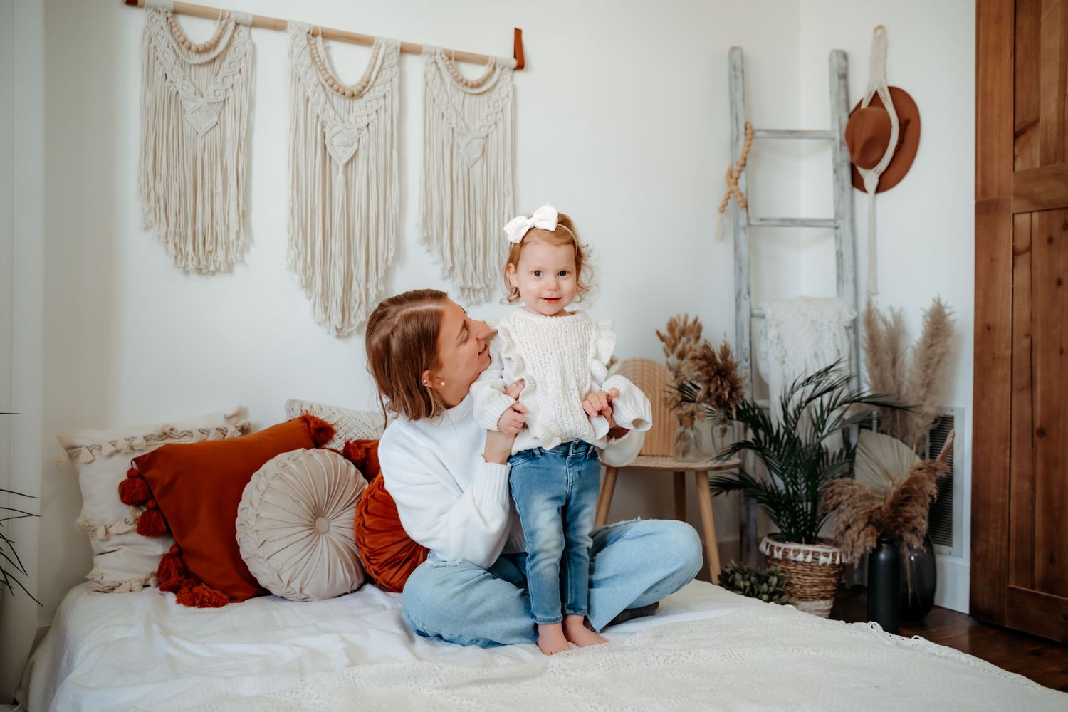 Macrame wall hangings decorate a cozy bedroom scene with bohemian decor including pillows and potted plants.