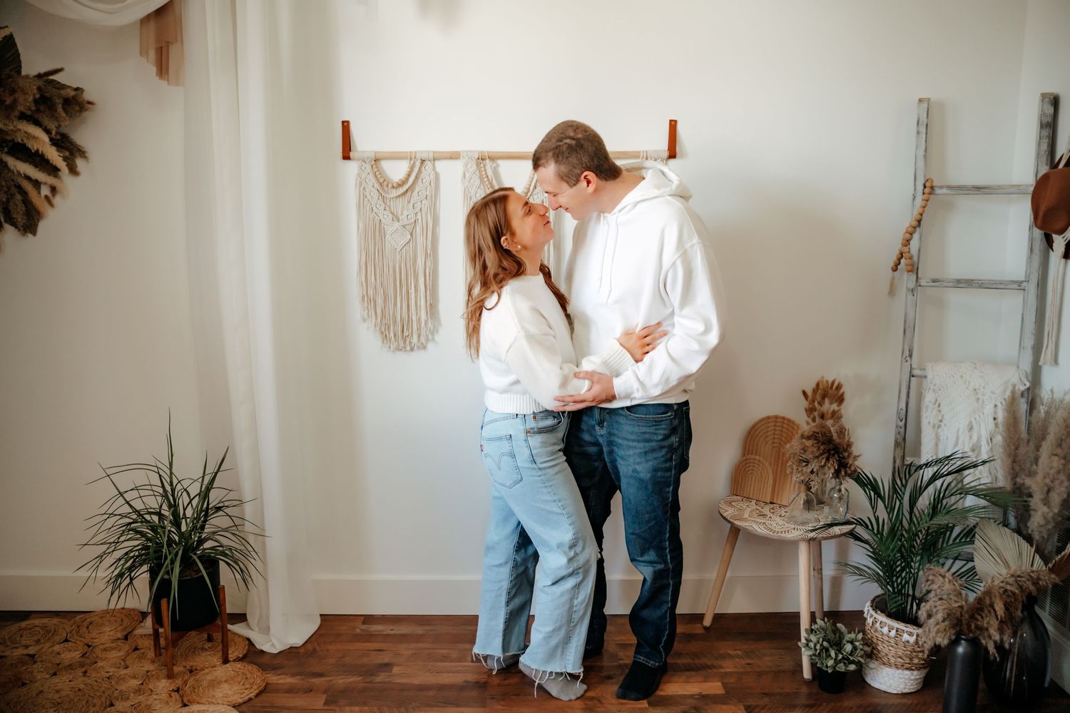 A couple shares an intimate moment in a cozy boho-style room with plants and macrame wall decor.