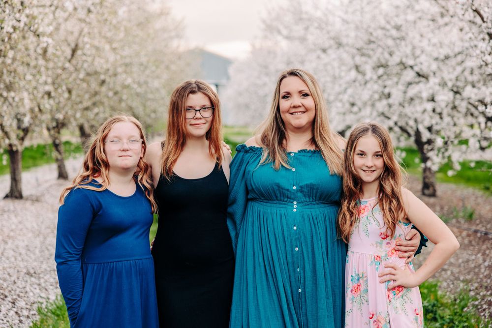 A group in coordinated blue and black dresses poses together in front of blooming spring cherry blossoms.