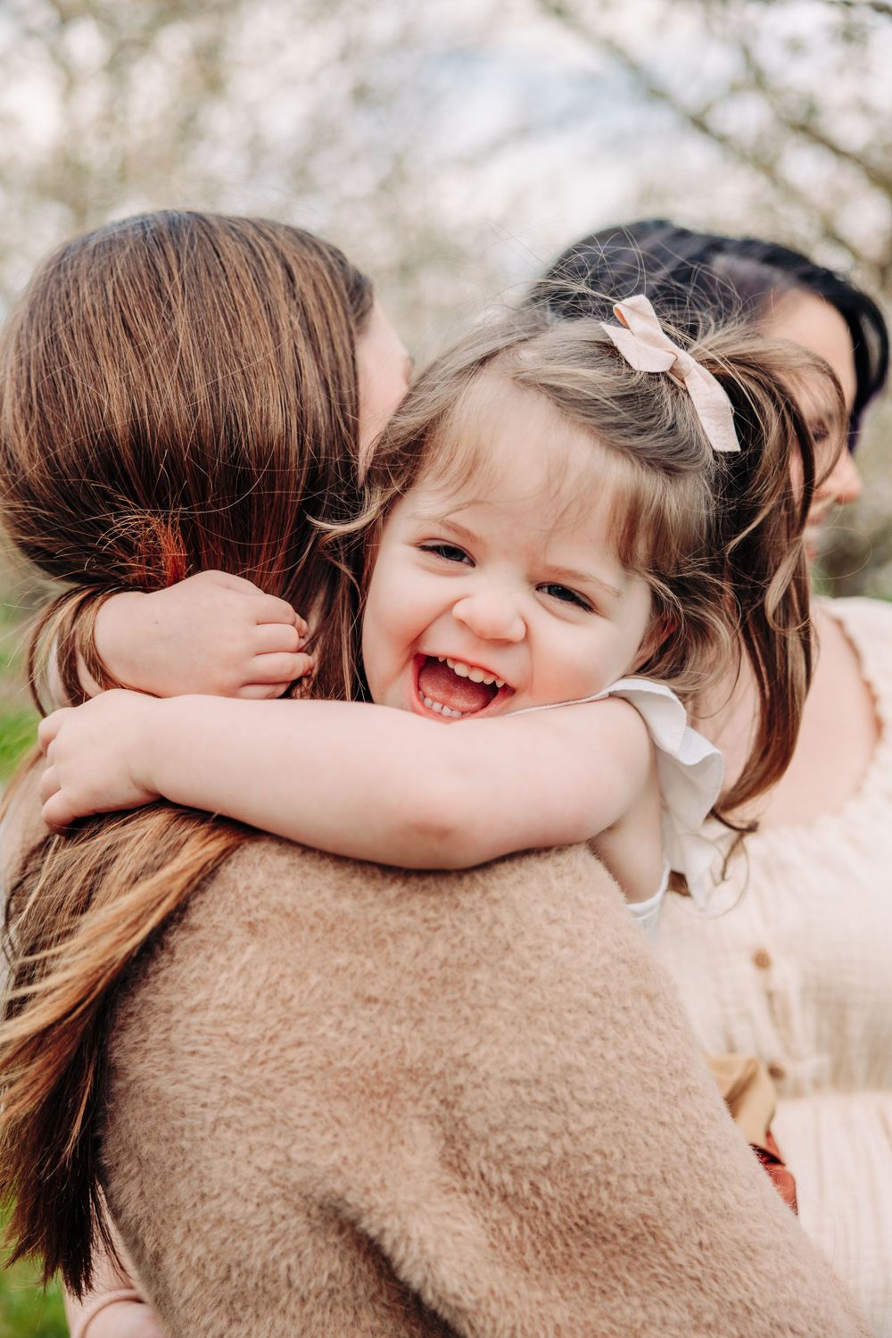 Pure joy and laughter captured during an outdoor embrace on a soft spring day with blurred blossoms in the background.