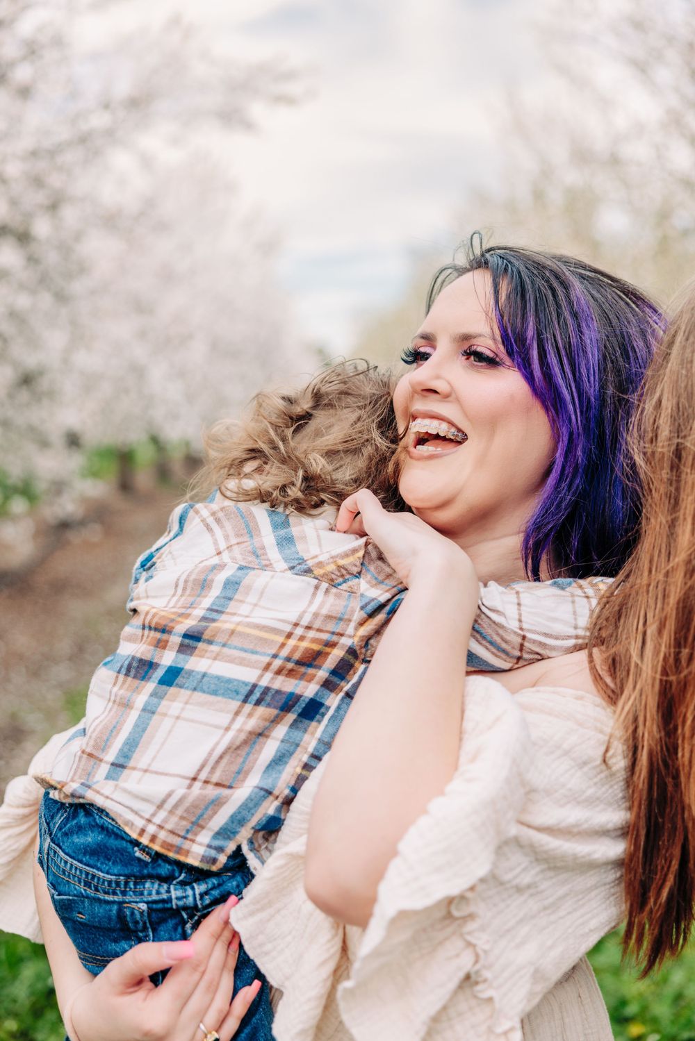 A candid moment of joy captured outdoors with blooming spring trees in the background while holding a small child.
