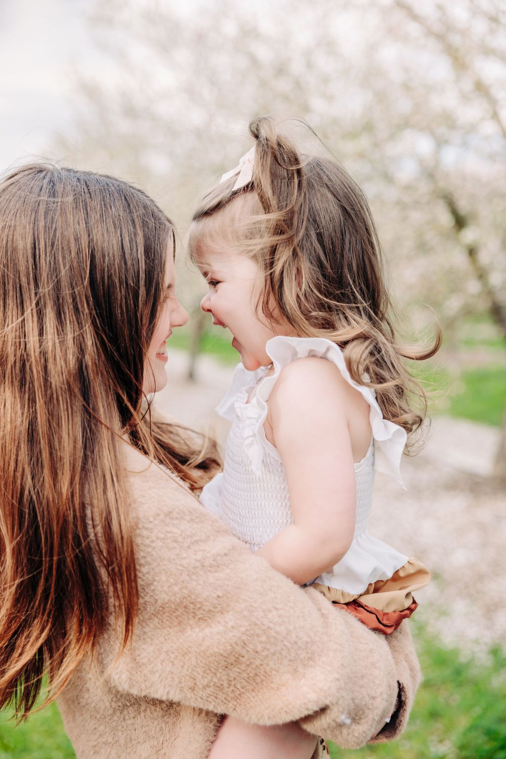 A tender moment shared between parent and child outdoors with blooming cherry trees in the background.