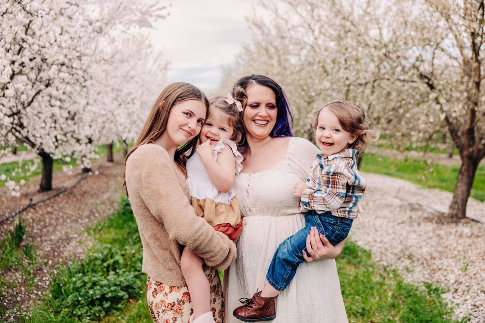 Beautiful family portrait in a blooming almond orchard on a spring day with white blossoms in the background.