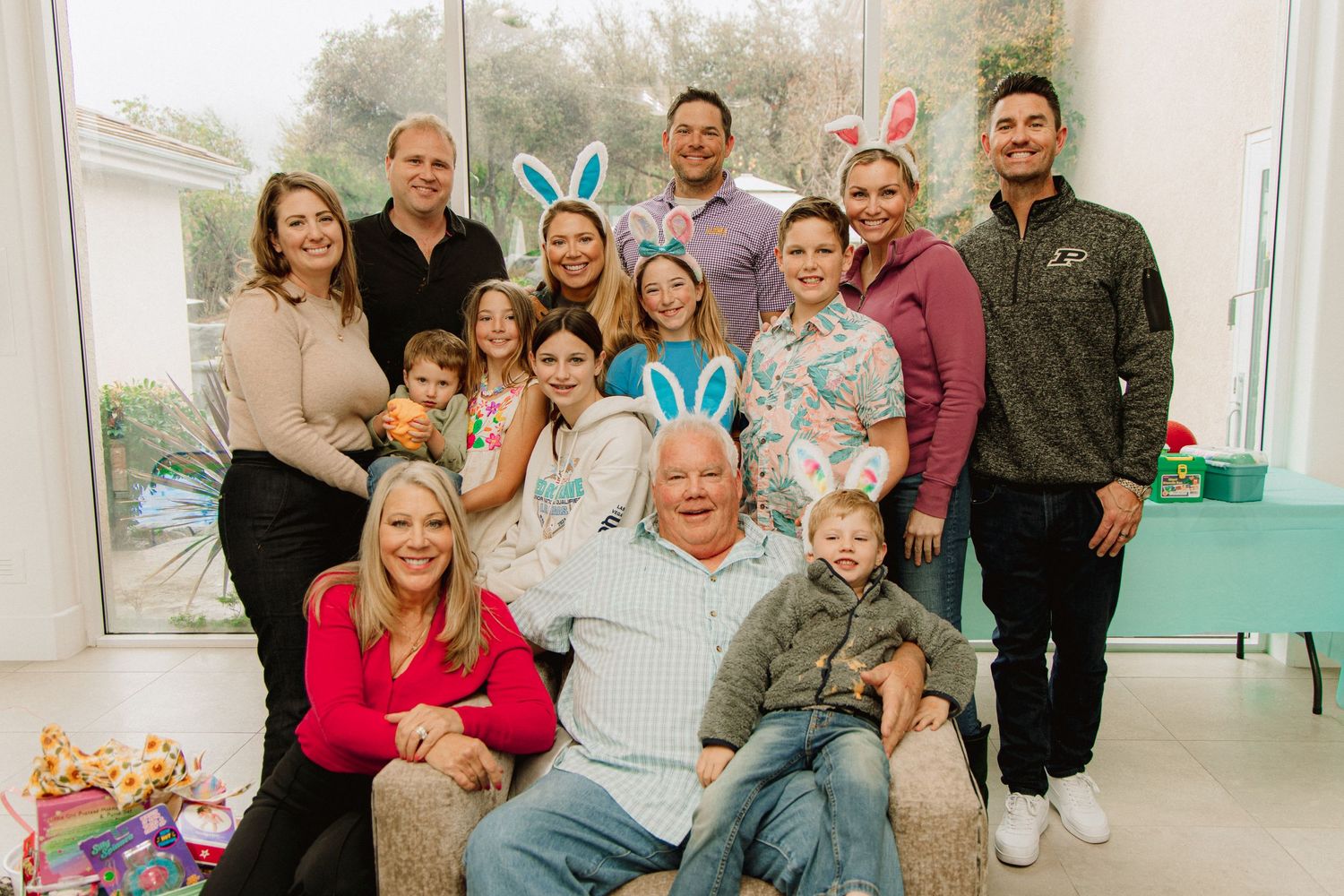 A large family group poses together for a holiday photo with blue bunny ears decorations in a bright indoor setting.