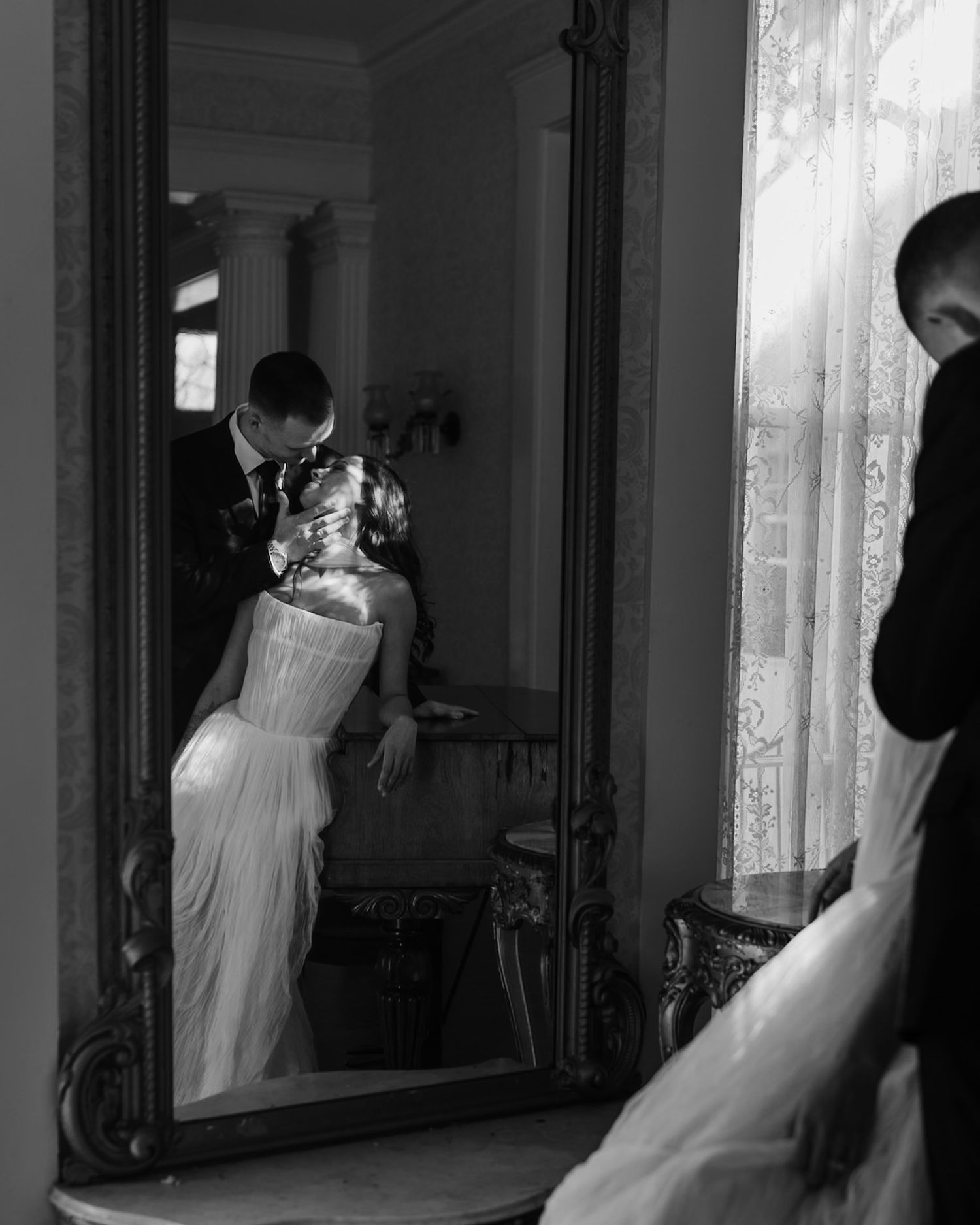 Romantic black and white reflection of couple embracing in ornate mirror.