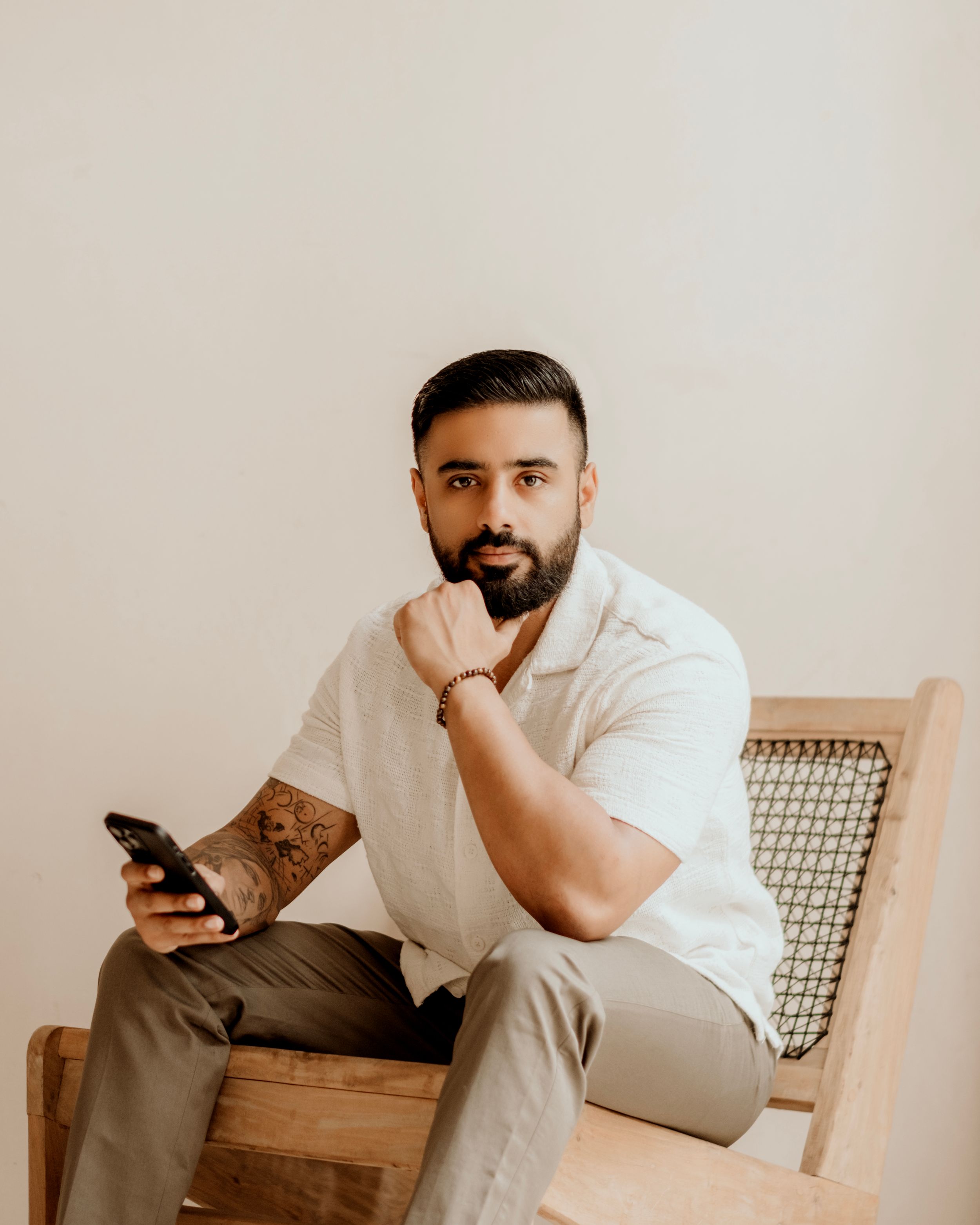 Figure in a rust-colored t-shirt and jeans sits thoughtfully on a stool against a neutral wall with framed art.