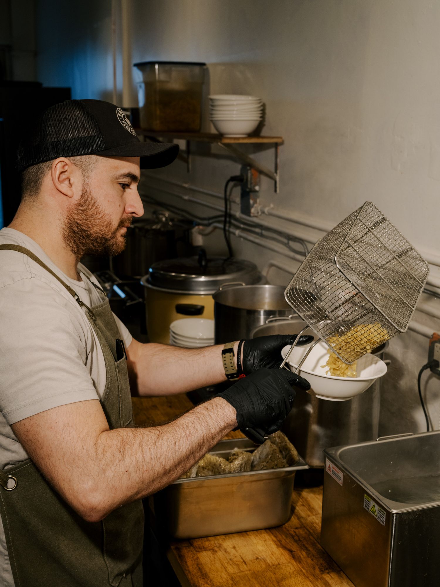 A cook preparing food in a restaurant kitchen while wearing an apron and black gloves.