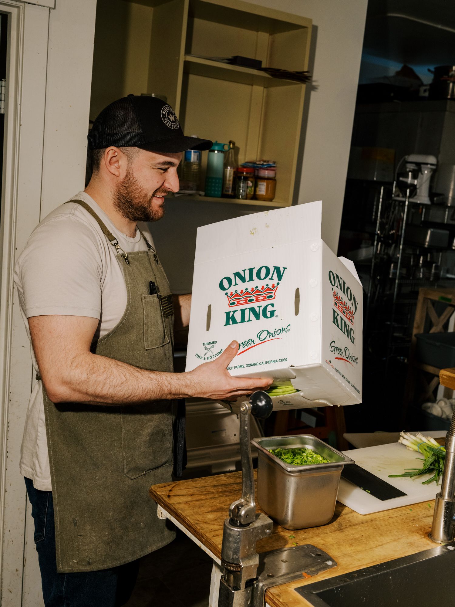 Restaurant worker in brown apron holding Onion King branded delivery box at prep station with food containers.