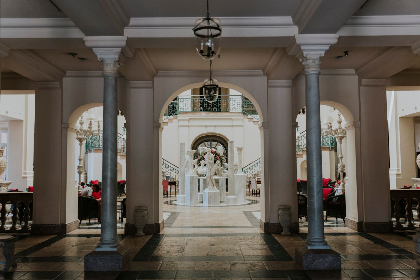 Elegant arched colonnade leads to ornate white baroque church interior with classical architectural details and hanging lantern.