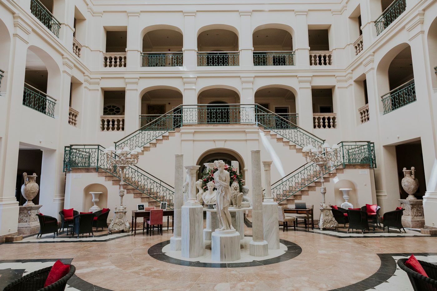 Elegant white marble courtyard with double curved staircases and classical sculptures in a luxury hotel atrium.
