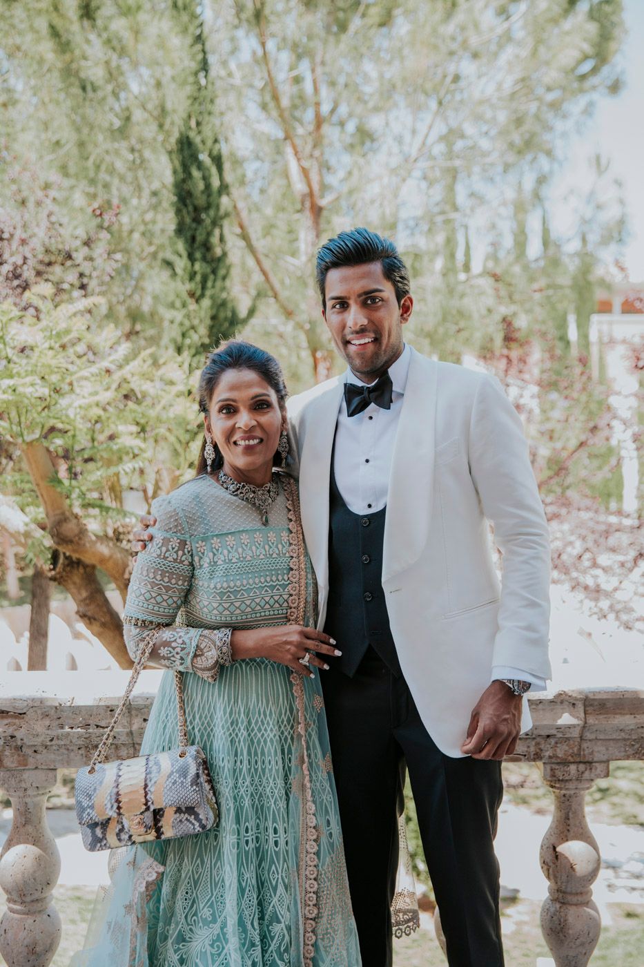 A couple poses in formal attire, with her in a mint green traditional dress and him in a white dinner jacket.