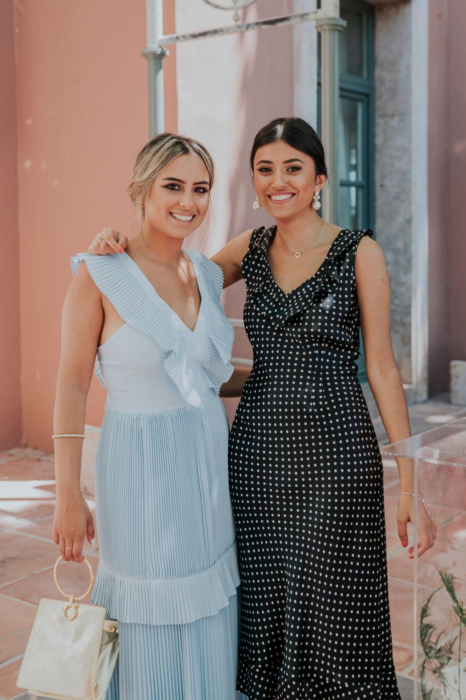 Two women posing in elegant dresses, one in light blue and one in polka dot pattern.