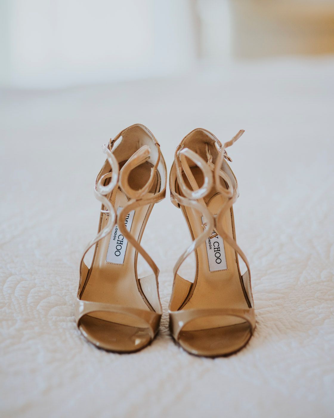 Elegant nude Jimmy Choo strappy sandals with stiletto heels displayed on white linen.