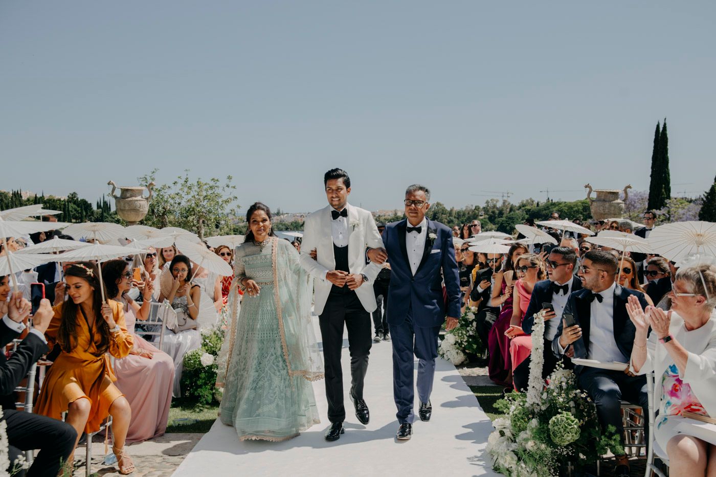 Wedding ceremony exit procession during an outdoor rooftop celebration with guests waving and cheering.