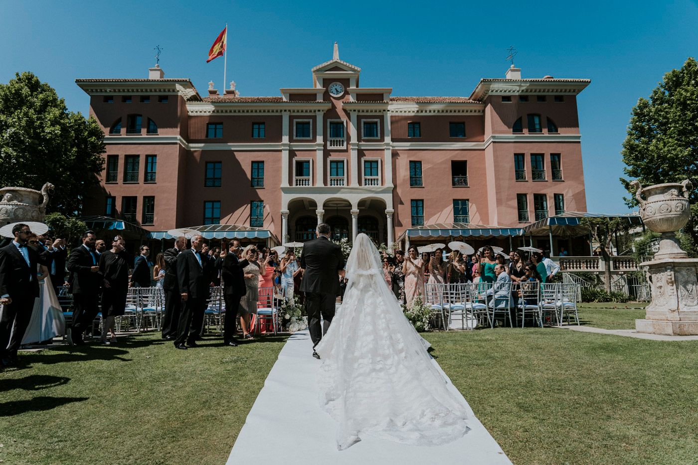A grand pink mansion with Italian-style architecture serves as an elegant backdrop for an outdoor wedding ceremony.