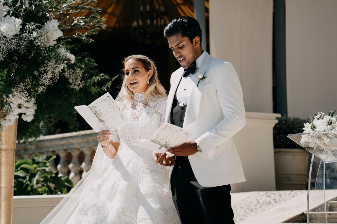 Bride and groom read papers together on an elegant terrace decorated with white floral arrangements.