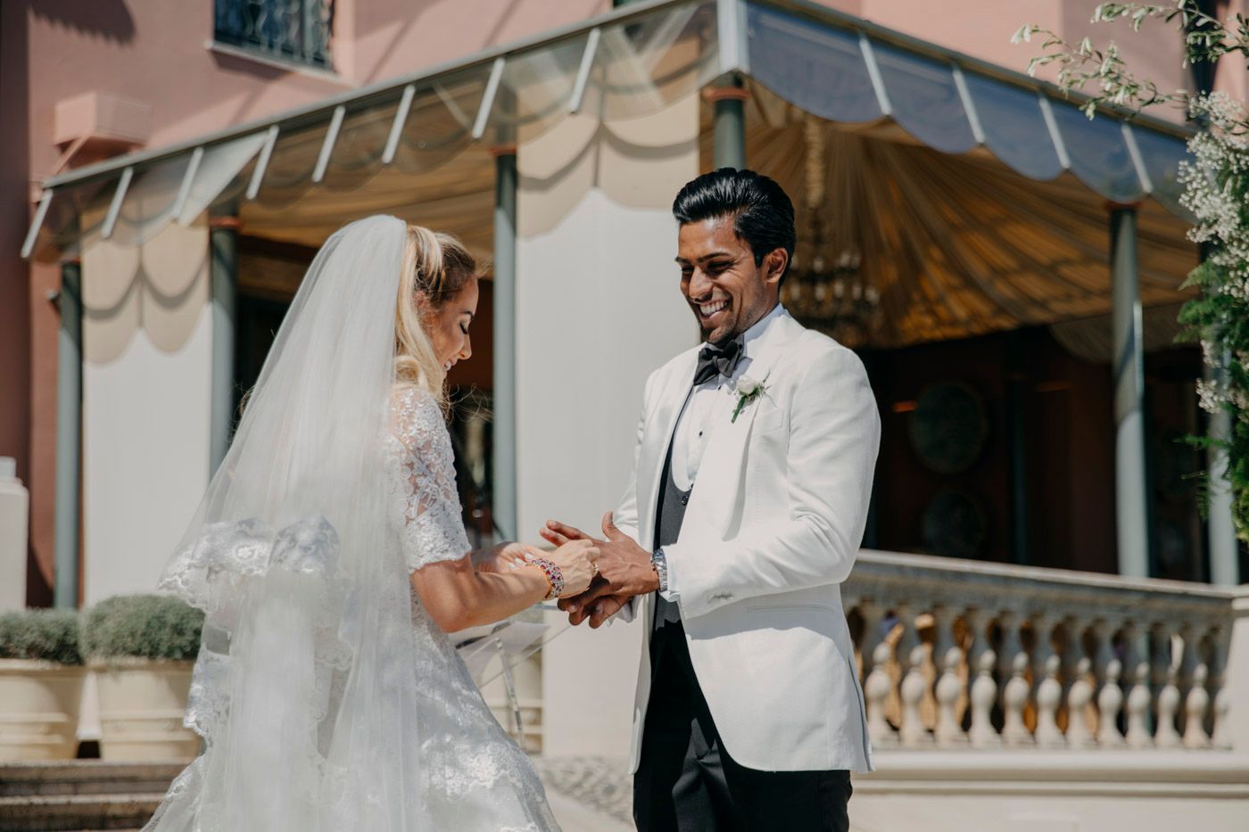 A romantic wedding ceremony moment takes place under an elegant covered porch with stone balustrades.