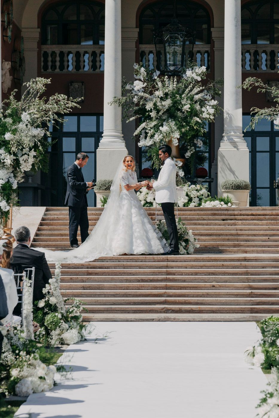 Elegant wedding ceremony on grand stone steps adorned with white floral arrangements and classical columns.