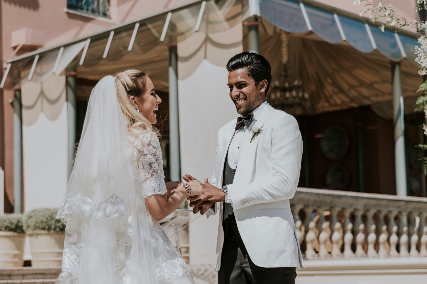 Two people exchanging rings during an elegant outdoor wedding ceremony in white formal attire.