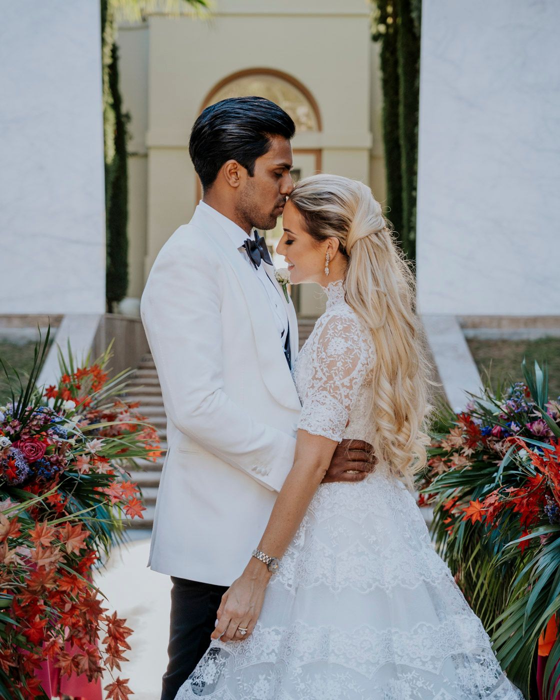 A romantic wedding portrait framed by vibrant red flowers and arched architecture.