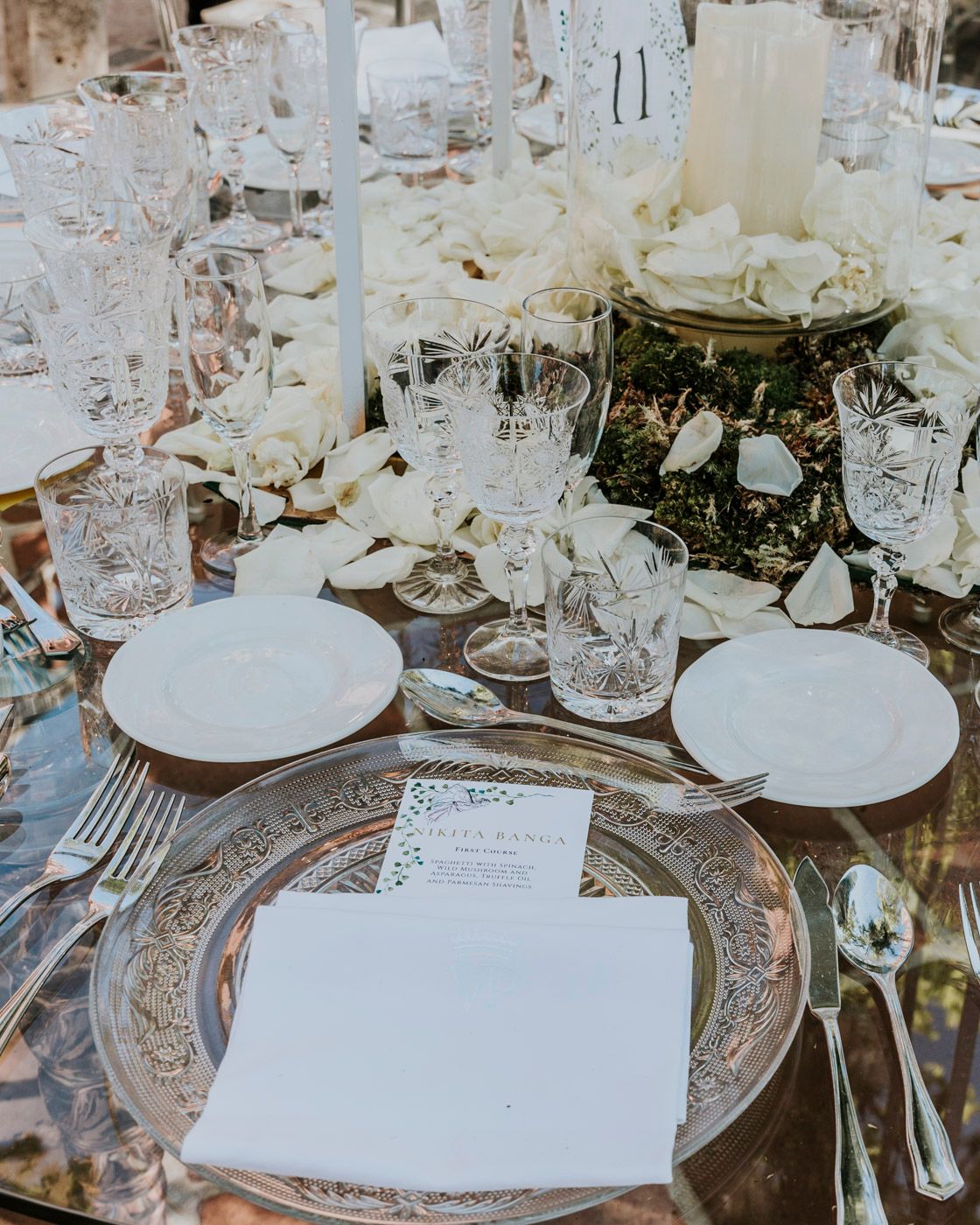 Elegant table setting with crystal glasses, white plates, and ornate silver chargers at a formal dinner event.