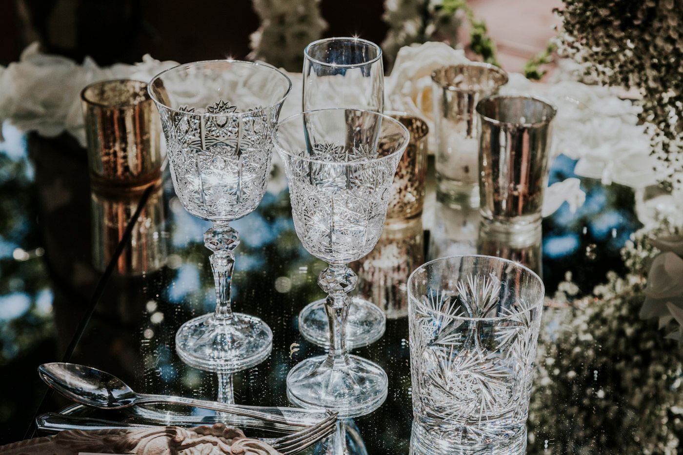 Vintage crystal glassware with intricate patterns arranged on an elegant table setting with floral decorations.