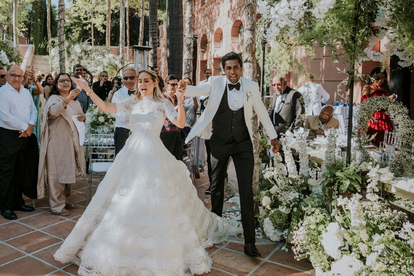A joyful couple celebrates during their outdoor garden wedding reception surrounded by floral arrangements and guests.