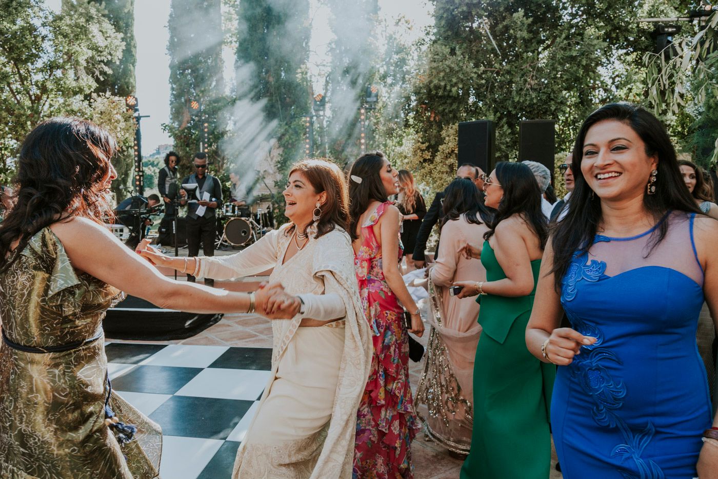Wedding guests dancing together on a checkered dance floor at an outdoor garden reception celebration.