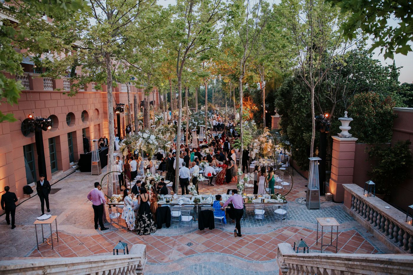 View from above of an elegant outdoor wedding reception with string lights and tables set up in a brick courtyard.
