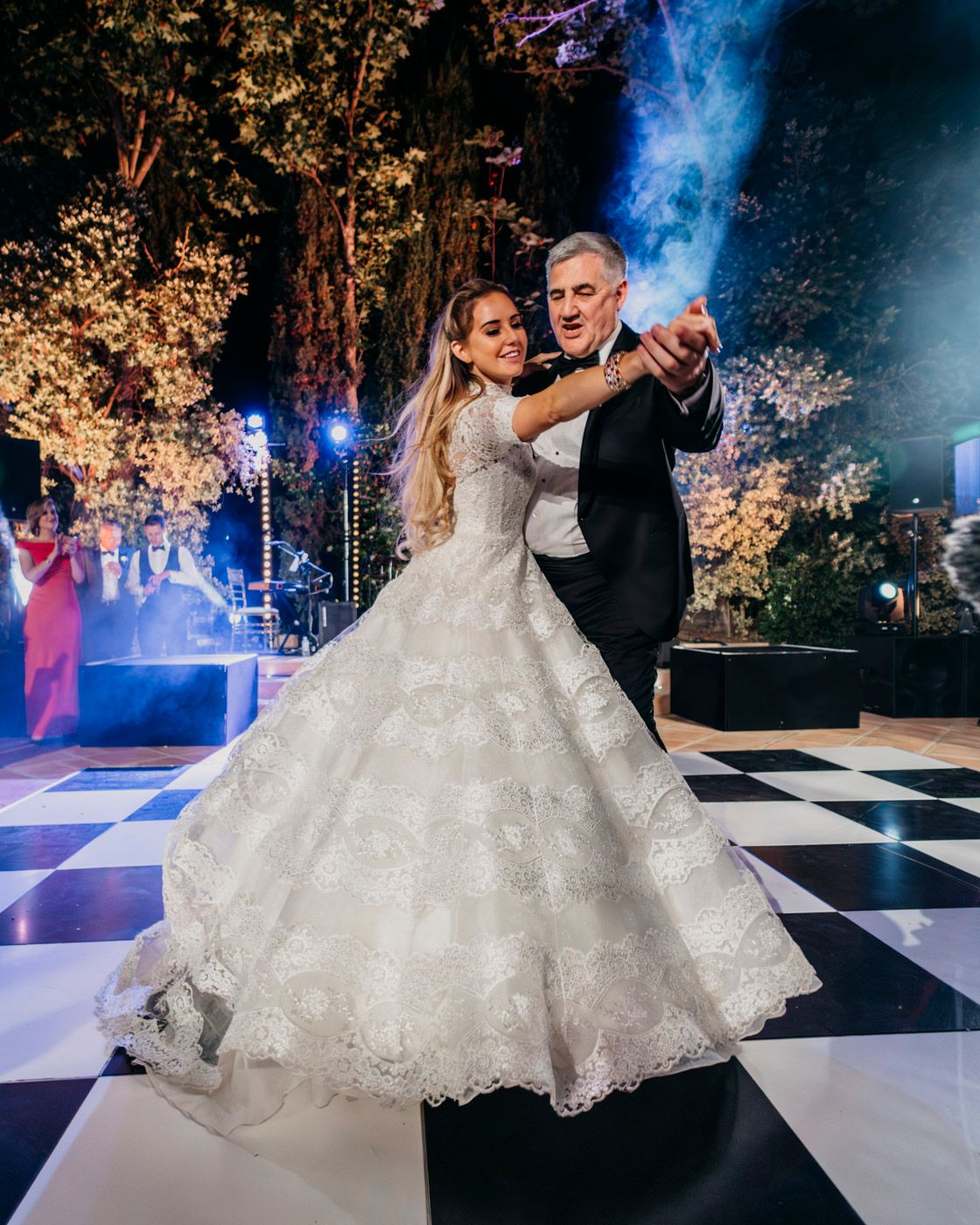 A couple shares their first dance at a wedding reception on a checkered dance floor with atmospheric lighting and smoke effects.