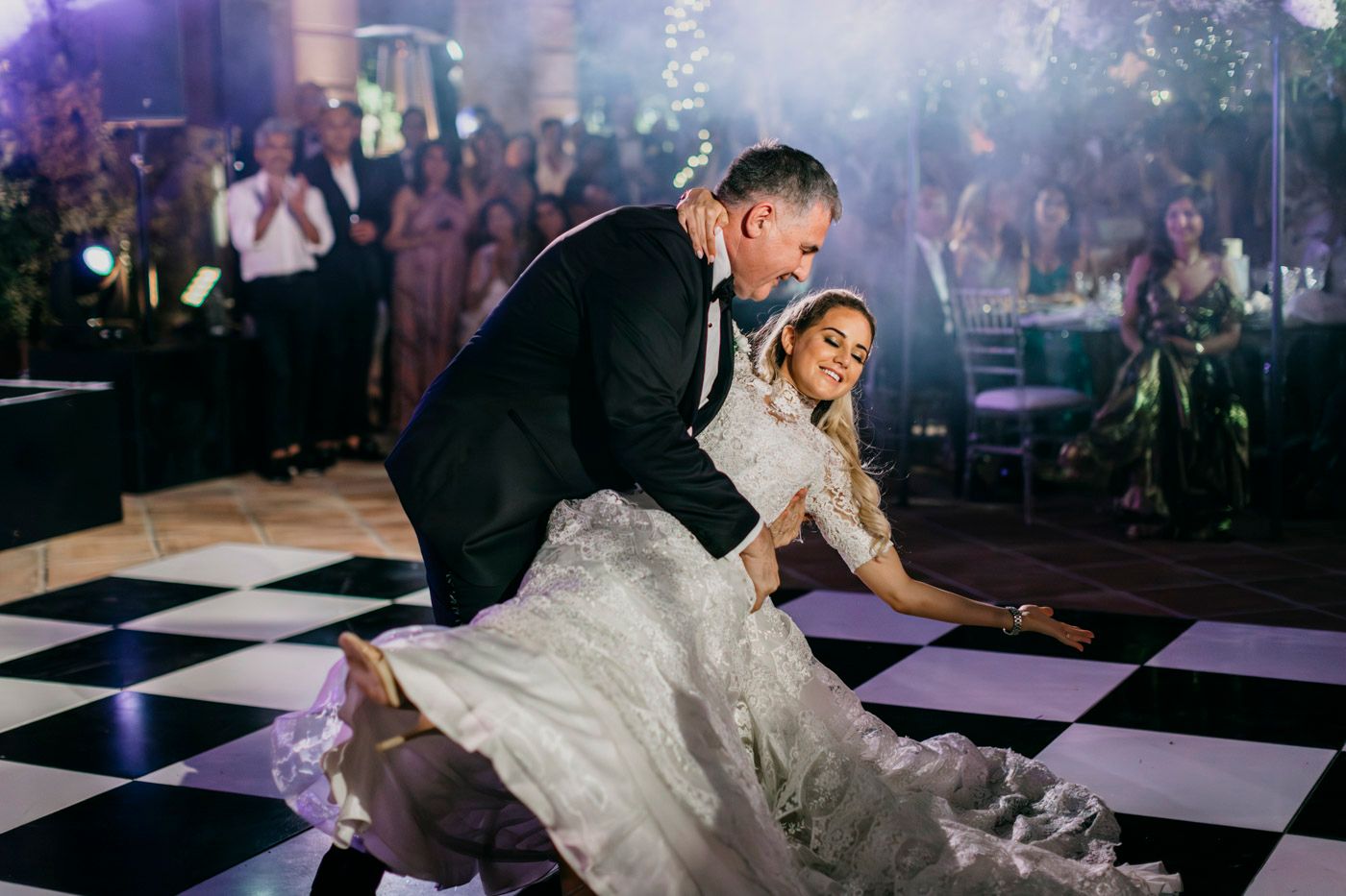 Couple performs romantic dip on black and white checkered dance floor at evening wedding reception.