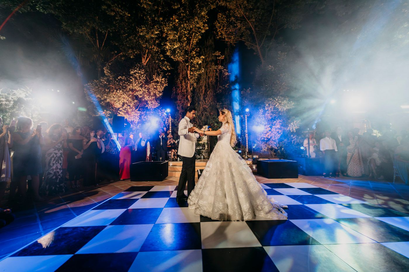 A romantic first dance on an illuminated checkerboard dance floor with blue lighting and dramatic fog effects at night.