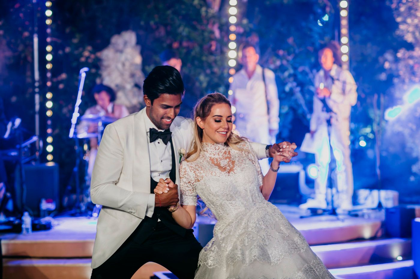 A joyful couple dances together at their wedding reception with band members visible in the background.
