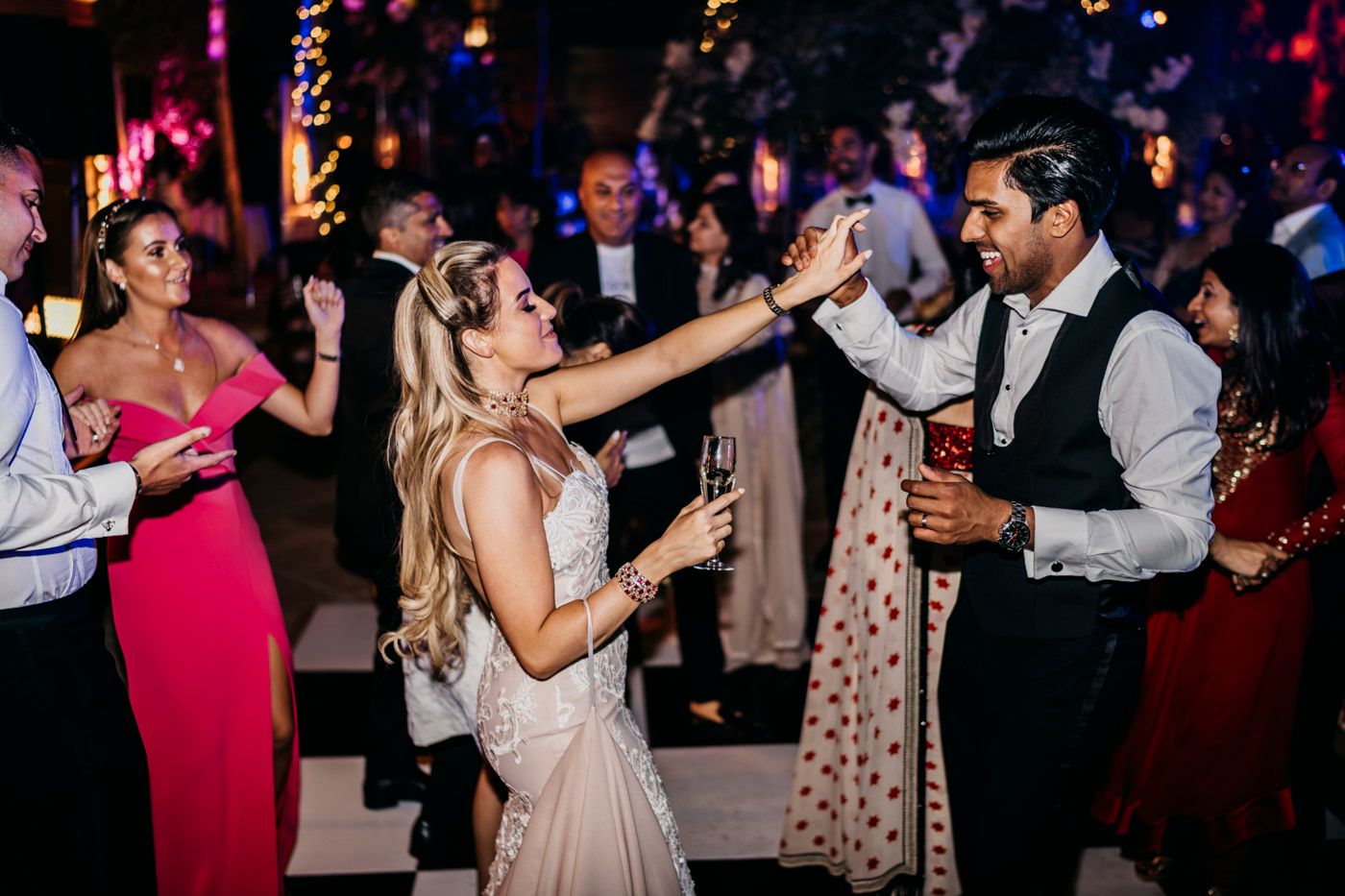 People dance and celebrate at a lively wedding reception with colorful lighting and festive atmosphere on the dance floor.