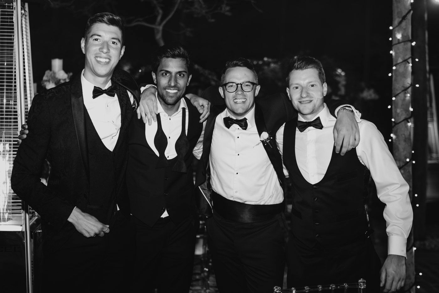 Four young men in formal attire pose together at an evening event in black and white vintage photograph.