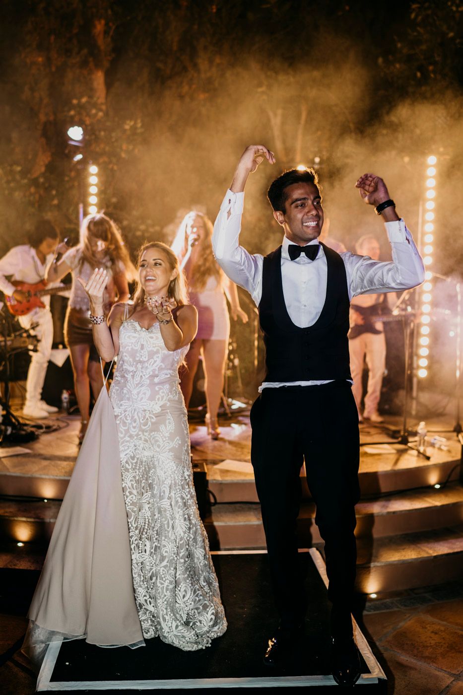 A couple celebrates on the dance floor at their wedding reception with a live band playing in the background.