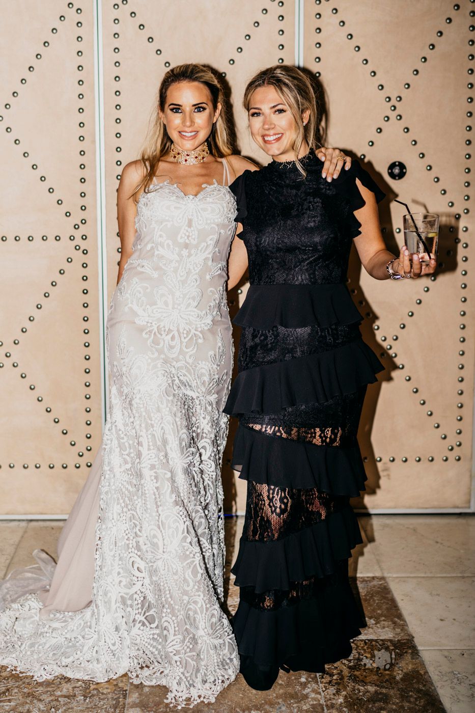 Two women pose together at an event wearing elegant lace dresses in white and black.