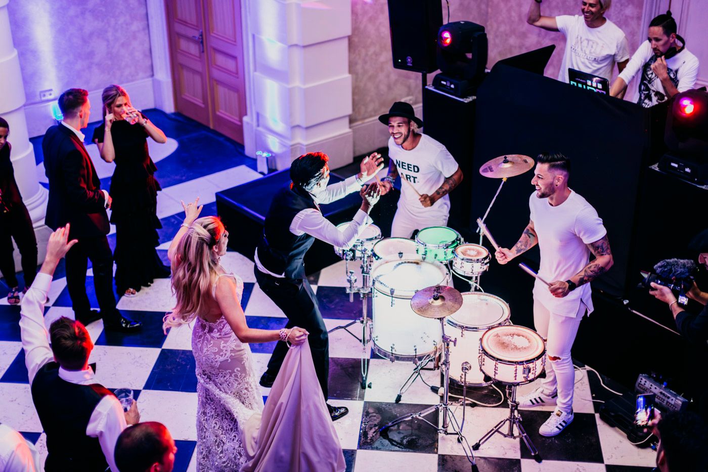 Live band performing on stage at an elegant wedding reception with people dancing to the music in a lavender-lit venue.