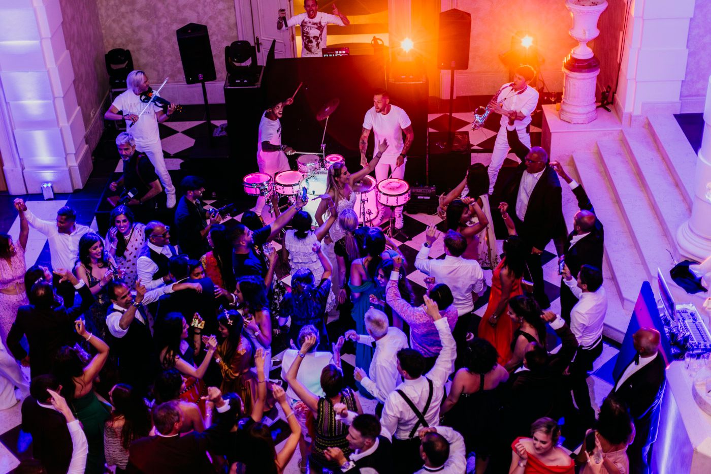 A crowded dance floor filled with party-goers dancing under vibrant purple and orange lighting at a nightclub event.