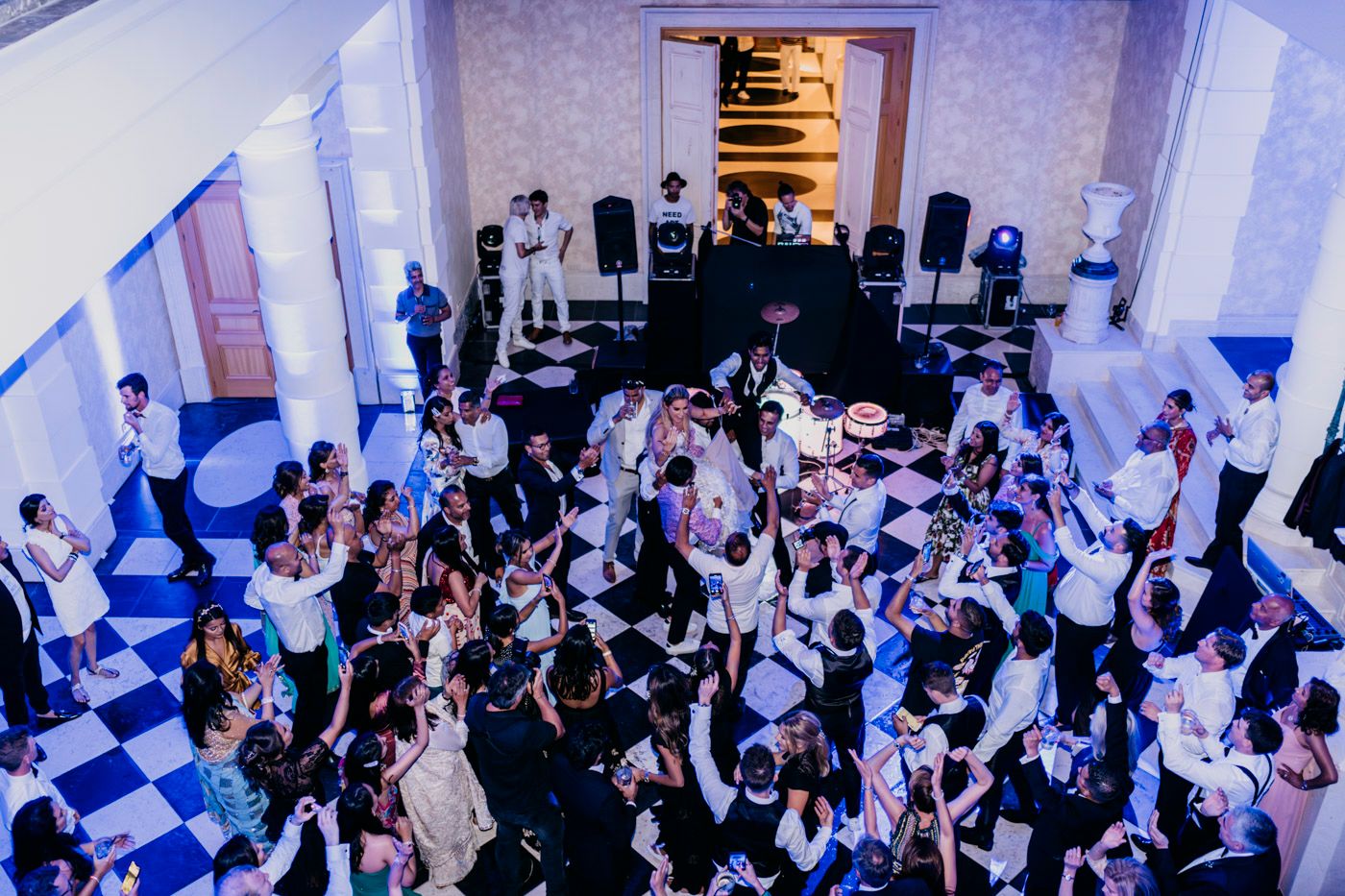 Aerial view of wedding guests dancing on a black and white checkerboard dance floor at an evening reception.