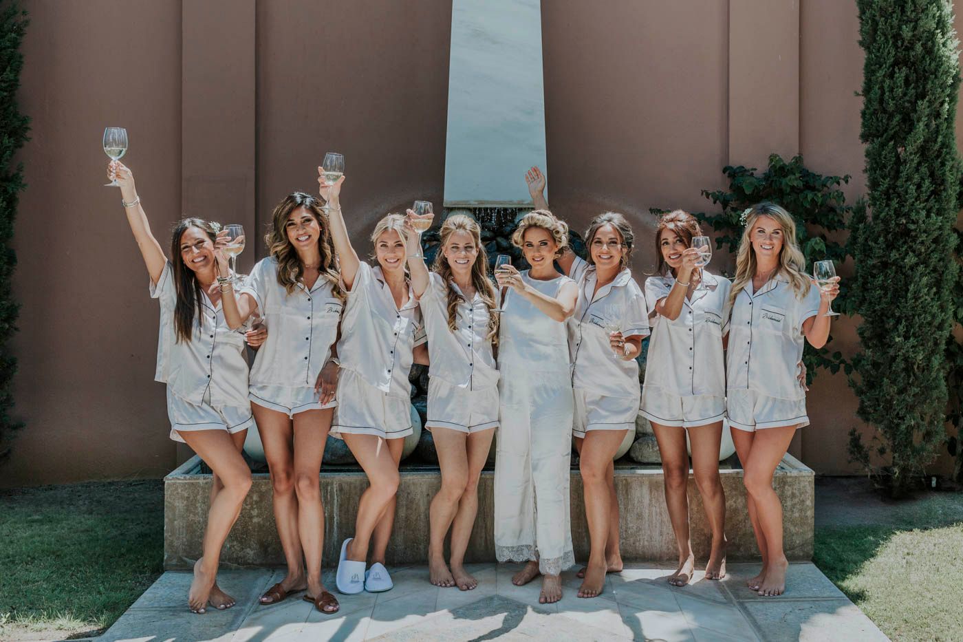 A group in matching light blue outfits pose together outdoors with raised arms in celebration.