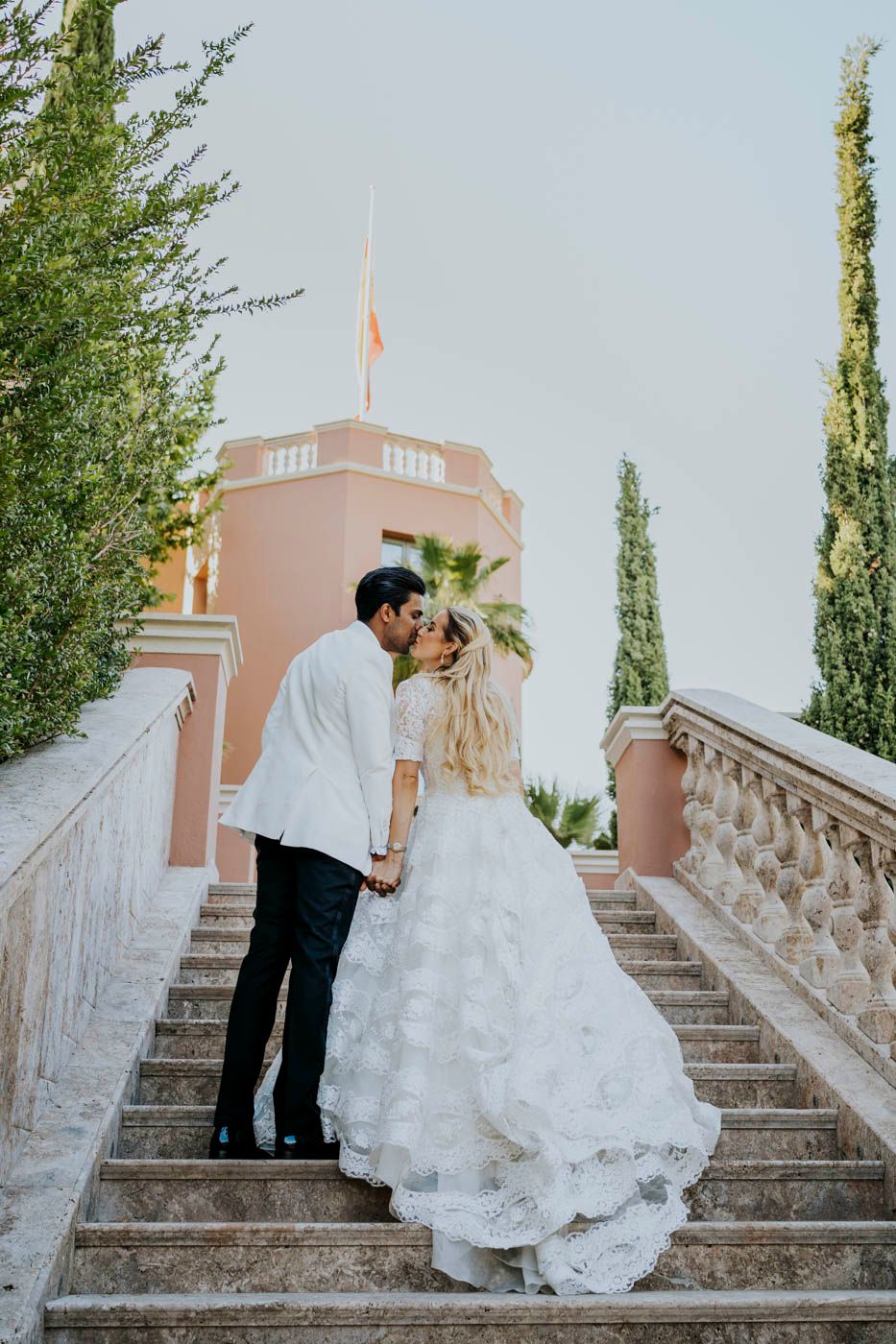 A romantic moment captured on marble steps with a pink tower and cypress trees framing the scene.