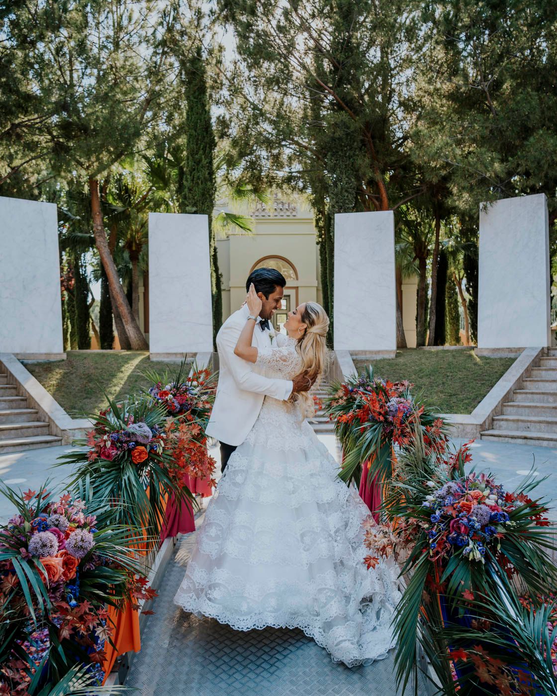 A couple sharing a romantic moment at a beautiful outdoor wedding ceremony with tropical floral arrangements and white pillars.