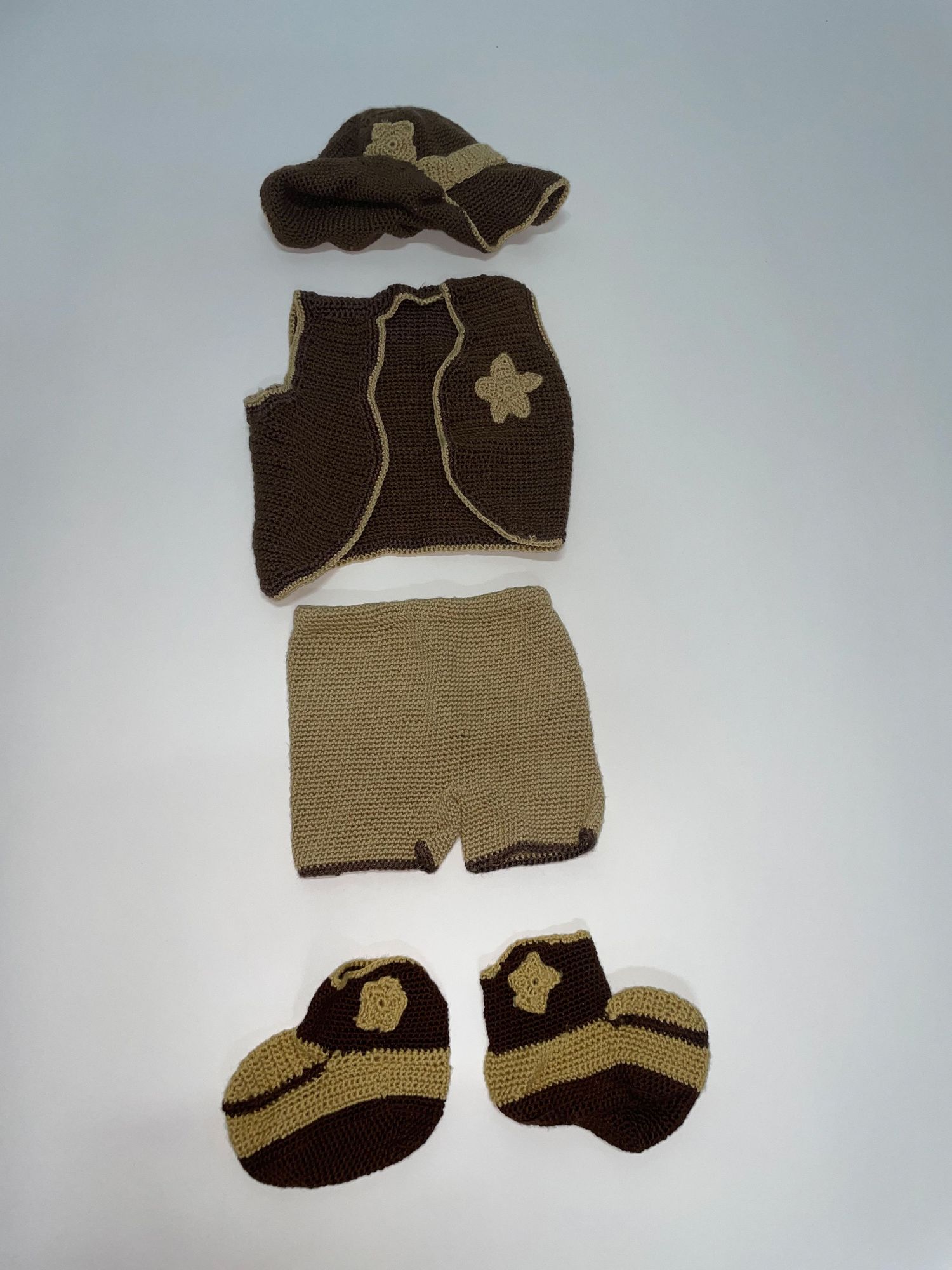 Brown and tan knitted baby outfit with boots and hat laid out on gray background.