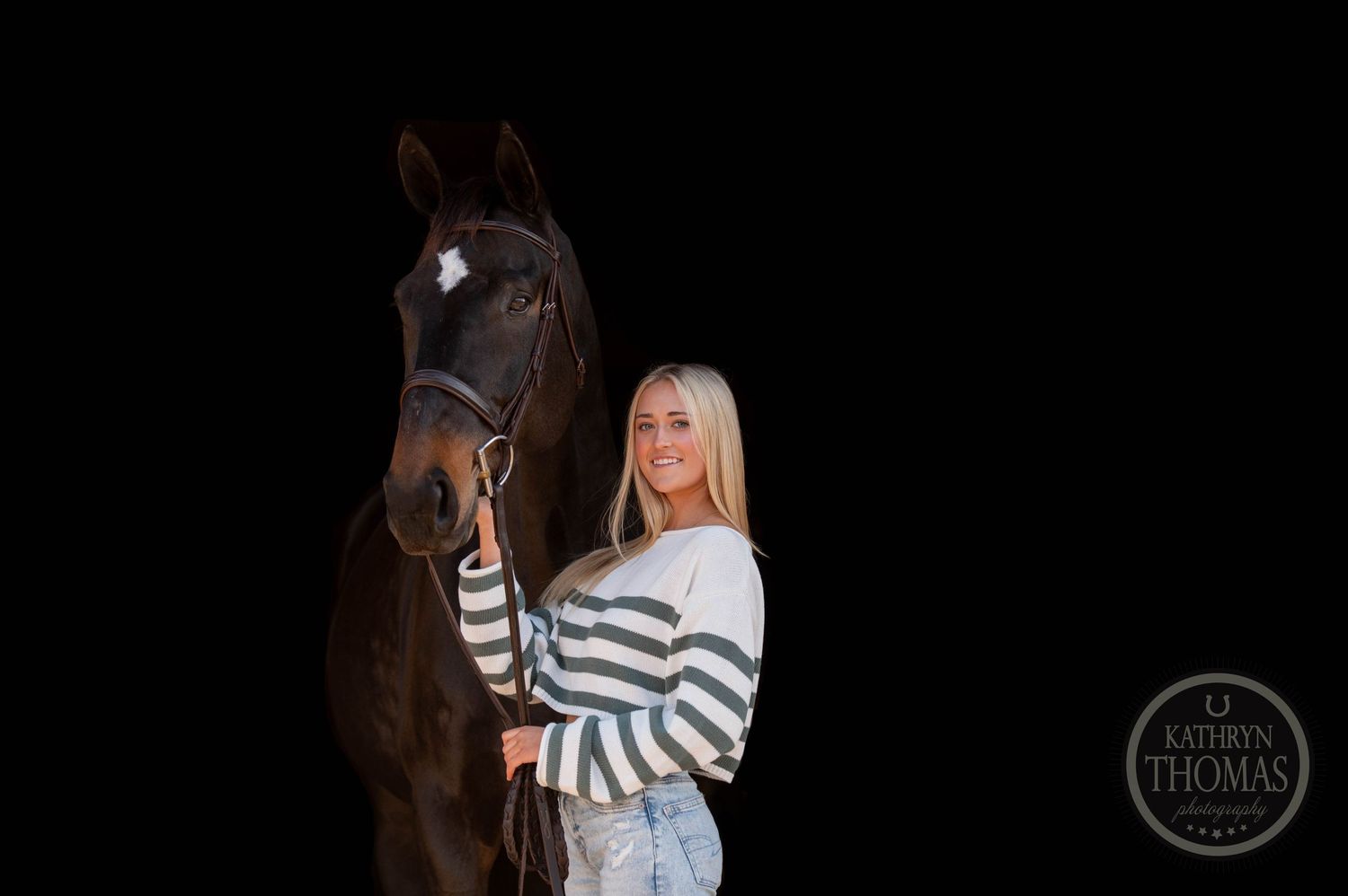 Dark brown horse and rider pose against black background in striped sweater.