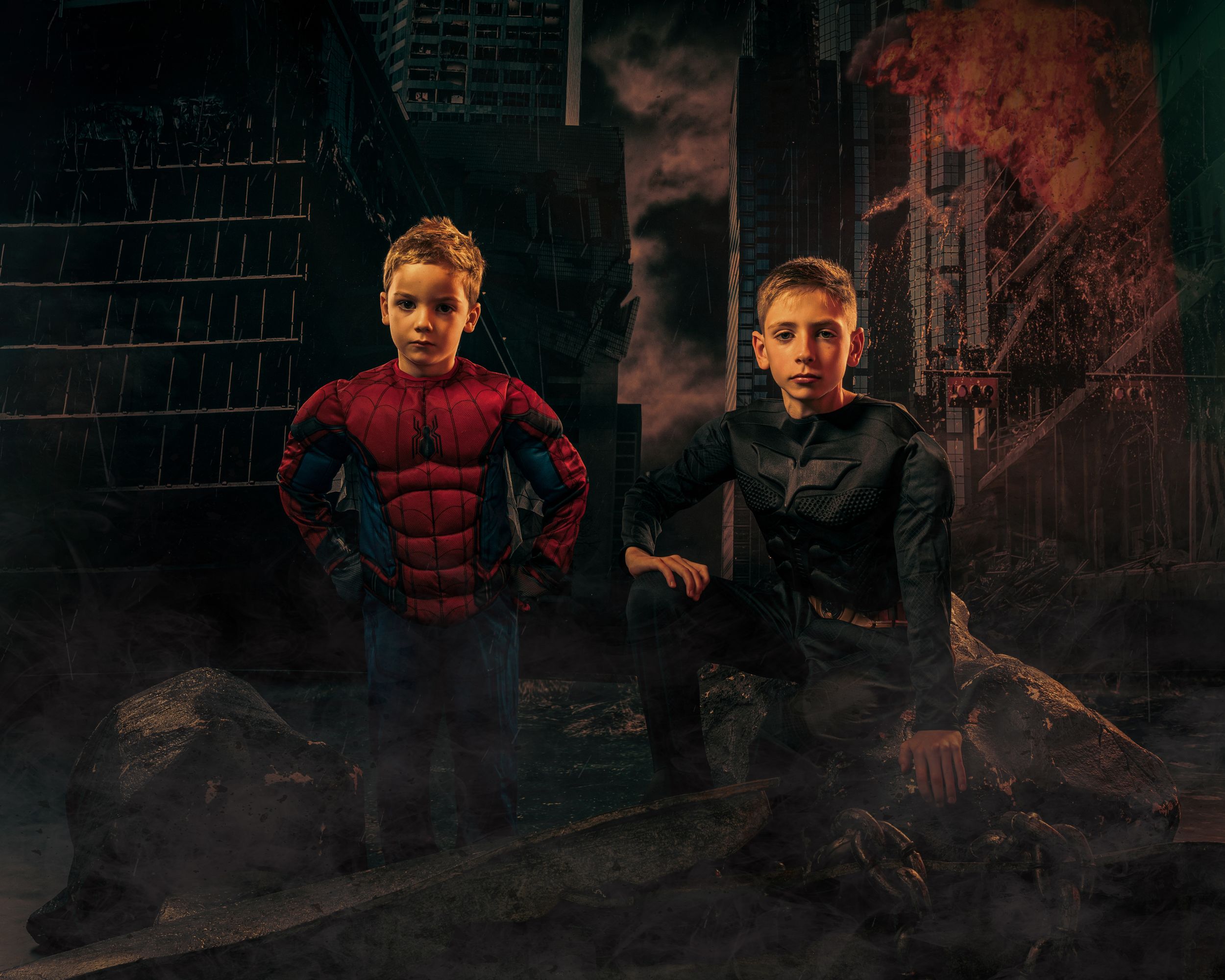 Two superheroes pose in a dark urban setting with burning buildings in the background.