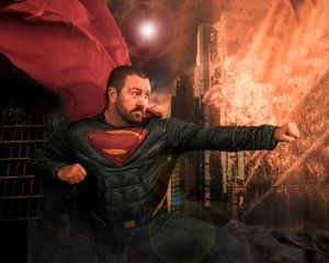 Dramatic Superman pose with flowing red cape against burning city backdrop.