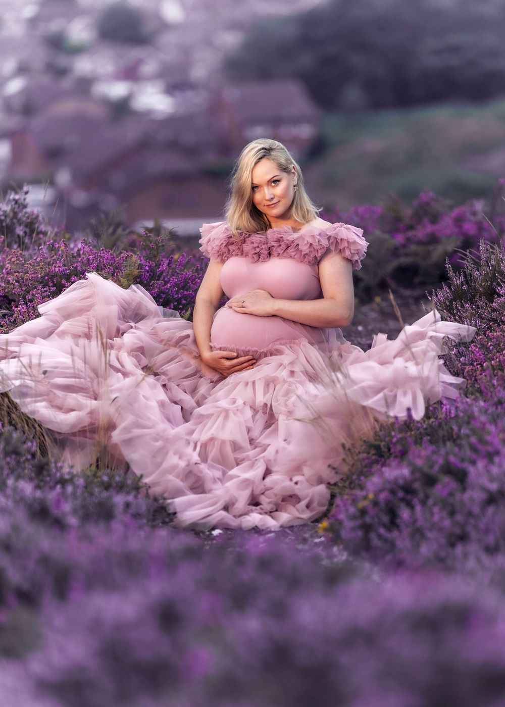Maternity portrait of woman in flowing pink gown sitting among purple lavender flowers.