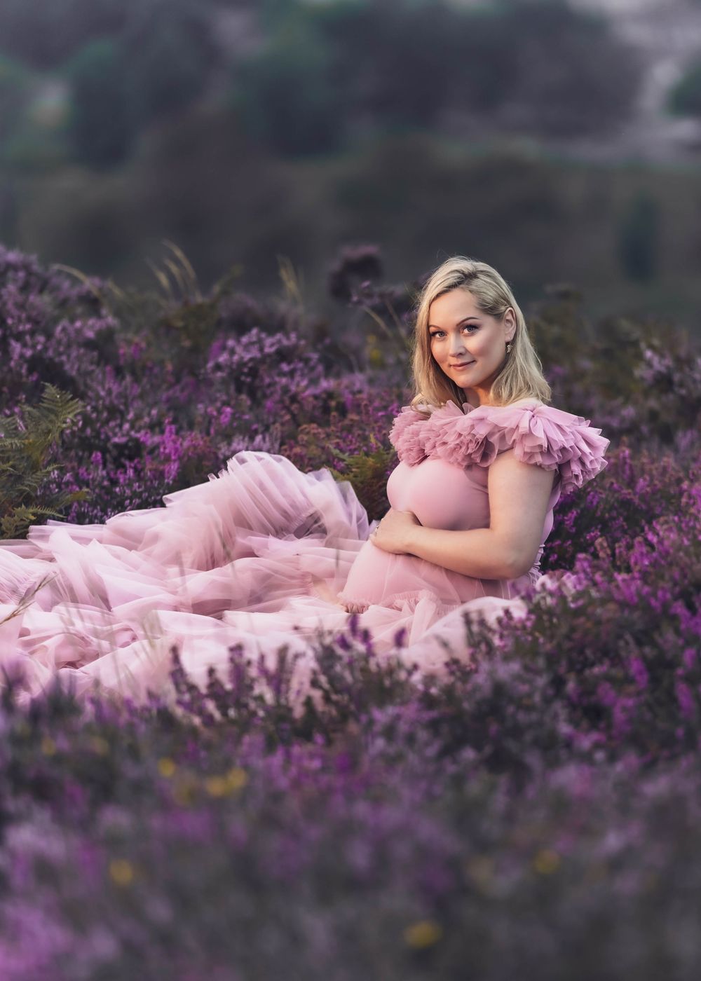 Expectant mother in pink dress reclining in field of blooming lavender.