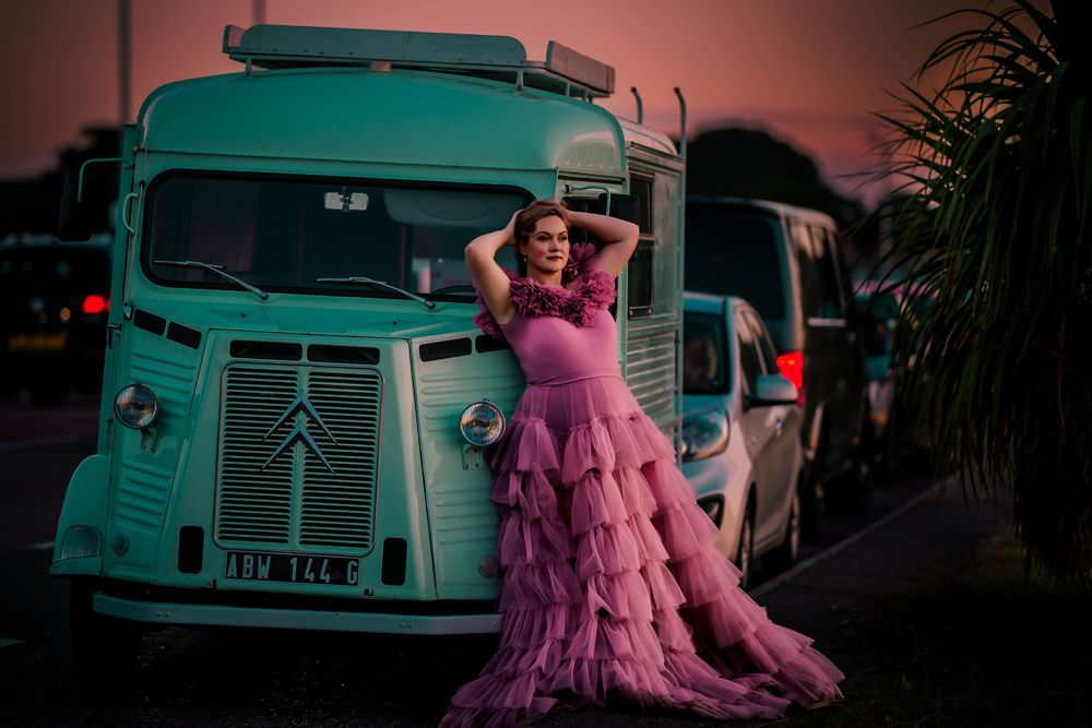 Woman in pink ruffle gown poses by vintage turquoise food truck for maternity photo.